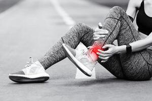 Sad Asian Girl Having Ankle Pain After Jogging In Park, Massaging Red Sore Spot, Sitting On Path, BW Style With Free Space photo