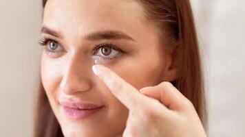 A young woman practices inserting a contact lens, demonstrating focus and precision. She uses her index finger to gently position the lens near her eye in a well-lit setting. photo