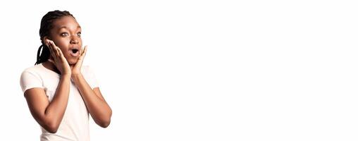 A young woman shows surprise with her mouth open and hands on her cheeks. Her reaction conveys disbelief and excitement, set against a clean white background in a studio setting. photo