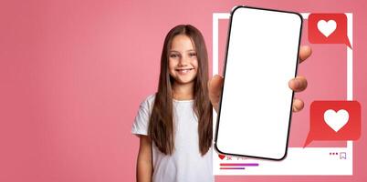 An influencer cute girl smiles while holding a smartphone in front of a pink background. She interacts with social media applications, inviting followers to like and chat. photo
