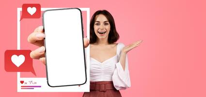 A lively influencer smiles and holds up a smartphone displaying a blank screen. She gestures expressively, promoting online interaction and social media engagement in a vibrant setting. photo