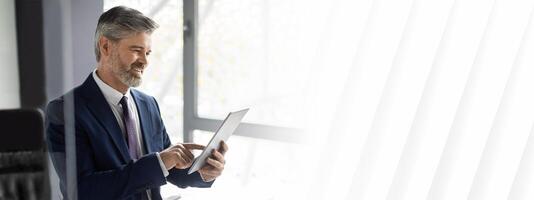 Successful Mature Businessman Using Digital Tablet At Workplace In Office, Happy Handsome Man Entrepreneur In Suit Browsing App On Modern Device, Enjoying Technologies For Business, Copy Space photo