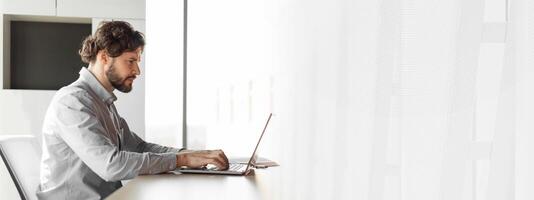 Side view of handsome mature businessman working at office, using laptop computer, sitting at desk, copy space. Man entrepreneur typing on pc keyboard, checking email, developing business strategy photo