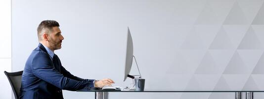 A middle aged Caucasian businessman is focused on his work at a sleek office desk. He engages with his computer, showcasing a professional environment perfect for productivity and success, copy space photo