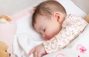 Baby girl sleeping in a cot with pacifier and toy photo