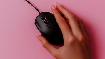 Hand using a black computer mouse on a pink surface photo