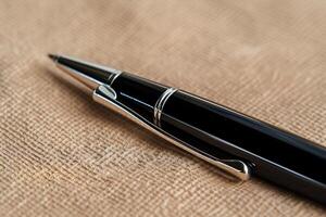 Close-up of a black pen on a beige fabric. The pen's tip and body are clearly visible, showcasing its metallic accents photo