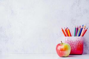 A red apple and a stack of colored pencils on a white table photo