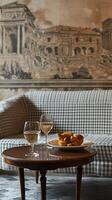 Elegant room with antique decor, featuring a sofa, table, and wine glasses. A vintage print of an ancient building is on the wall. A small plate of pastries rests on the table photo