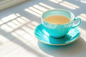 Delicate turquoise porcelain teacup and saucer set on a wooden table in soft morning light photo