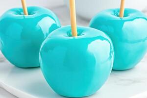 Glossy turquoise candy apples arranged on a marble surface with soft reflections creating a vibrant and delightful dessert display photo