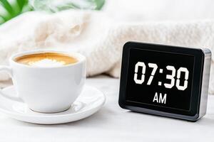 Retro digital flip clock displays 07.30 AM next to a steaming cup of coffee on a minimalist bedside table in a serene morning setting photo
