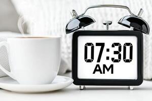 Retro flip clock showing 07.30 AM near a steaming cup of coffee on a minimalist bedside table for a peaceful morning setup photo