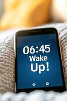Smartphone alarm screen displaying wake up message at 06.45 with soft morning light reflecting on a cozy bed photo
