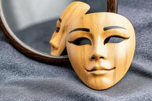 Symbolic composition of a wooden mask on a vanity table with a distorted reflection in a mirror, representing themes of identity and vanity in contemporary context photo