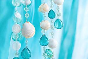 Swaying bohemian wind chime with glass beads and seashells against turquoise drapes in a sunlit coastal decor setting photo