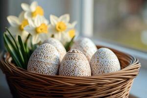 Easter eggs with white icing decorations lying in wicker basket near daffodils by window photo