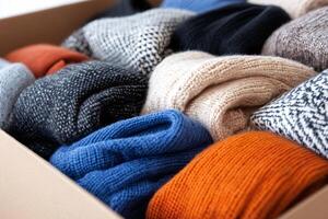 Warm knitted sweaters are neatly folded and stored in a cardboard box photo