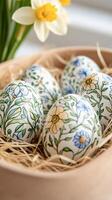 Easter eggs with floral pattern resting in a bowl with daffodils in background photo