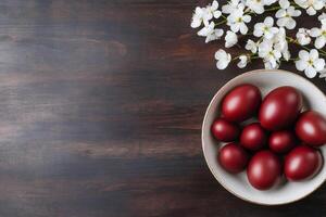 Easter eggs painted in red color lying in a bowl near cherry blossom on dark wooden background photo