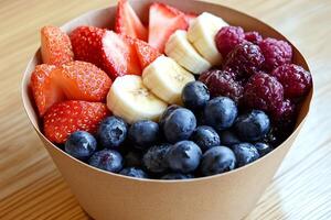 Paper bowl full of fresh strawberries, banana slices, blueberries and raspberries creating a colorful and healthy meal photo
