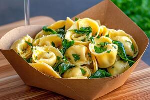 Tortellini with parmesan and spinach resting in a cardboard container photo