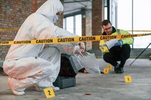 Woman holds ,the sleeve from the cartridge and puts it in the bag. Detectives are collecting evidence in a crime scene near dead body photo