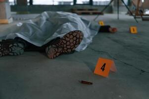 Bullet shell as clue. Dead body of a man is on the ground, covered in white cloth. Conception of murder, homicide photo