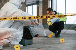 Woman, holds the sleeve from the cartridge and puts it in the bag. Detectives are collecting evidence in a crime scene near dead body photo