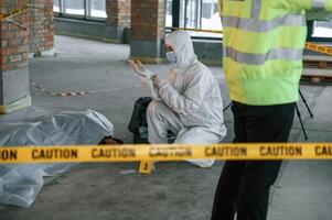 Woman is putting on the gloves. Detectives are collecting evidence in a crime scene near dead body photo