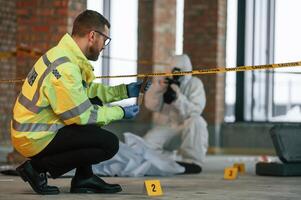 Woman is using camera,, making photos. Detectives are collecting evidence in a crime scene near dead body photo