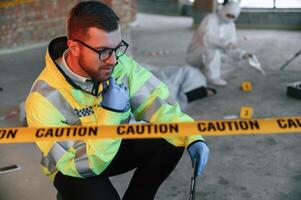 Sitting ,near, caution police tape. Detectives are collecting evidence in a crime scene with dead body photo