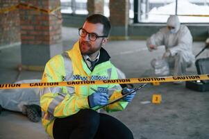 Sitting, near caution police tape. Detectives are collecting evidence in a crime scene with dead body photo