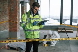 Man, writing information into notepad. Detectives are collecting evidence in a crime scene near dead body photo