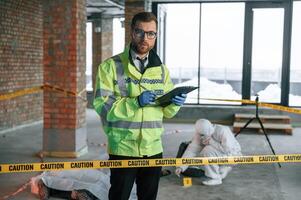 Man writing information into notepad. Detectives are collecting evidence in a crime scene near dead body photo