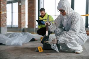 Knive and blood is on the ground. Detectives are collecting evidence in a crime scene near dead body photo