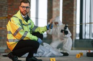 Woman is ,using camera, making photos. Detectives are collecting evidence in a crime scene near dead body photo