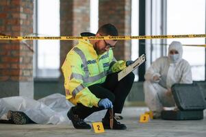 Knife clue. Detectives are collecting evidence in a crime scene near dead body. Forensic specialists are making expertise photo