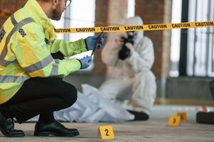 Woman is, using camera, making photos. Detectives are collecting evidence in a crime scene near dead body photo
