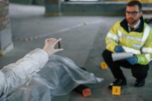 A woman is holding a shell casing. Detectives are collecting evidence in a crime scene near dead body photo