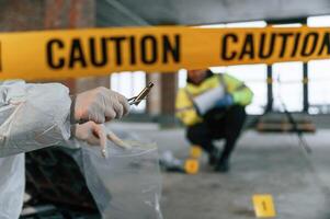 Woman holds the sleeve from the cartridge and puts it in the bag. Detectives are collecting evidence in a crime scene near dead body photo