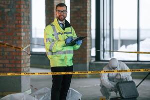 Man is, standing and smiling. Detectives are collecting evidence in a crime scene near dead body photo