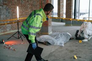Detectives, are collecting evidence in a crime scene near dead body. Forensic specialists are making expertise photo