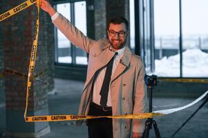 Positive detective in coat is holding caution police tape and smiling photo
