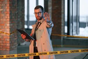 Stop gesture.. No trespassing.. Male detective in coat is collecting evidence in a crime scene on the construction site photo