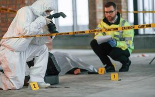 Woman is making photos ,by camera. Detectives are collecting evidence in a crime scene near dead body