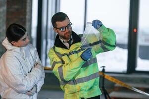 Holding knife i,n package. .Two detectives are collecting evidence in a crime scene photo