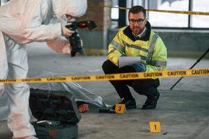 Woman is, making photos by camera. Detectives are collecting evidence in a crime scene near dead body