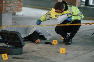Male detective is ,collecting evidence, in a crime scene near dead body on the construction site photo