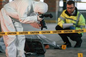 Woman is making photos by ,camera. Detectives are collecting evidence in a crime scene near dead body